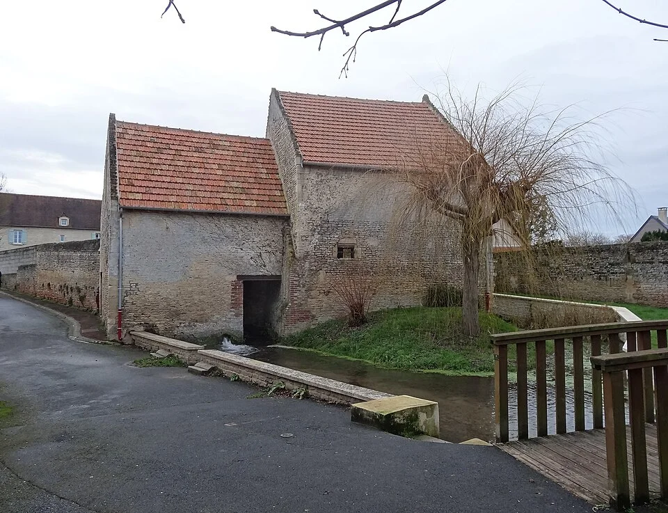 L’ancien moulin et le pont sur la Mue à Cairon. Vue de la commune ; la bibliothèque des Tilleuls n’est pas représentée.